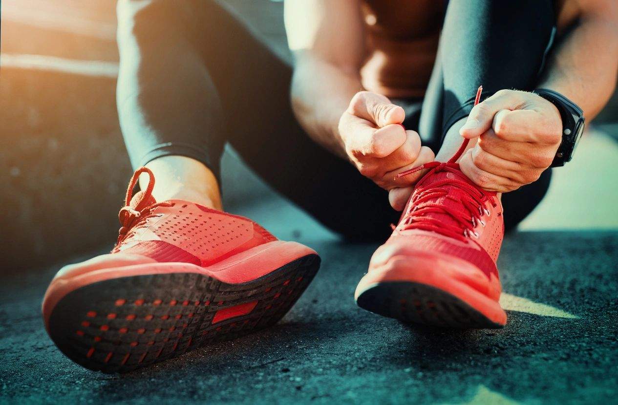 A person ties their shoes on the ground.