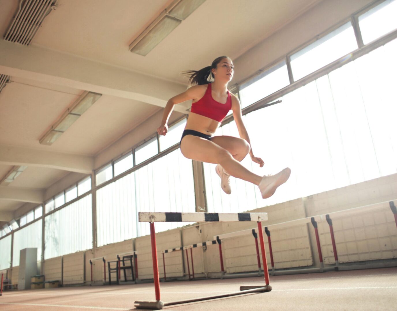 A woman jumping over an obstacle in the gym.